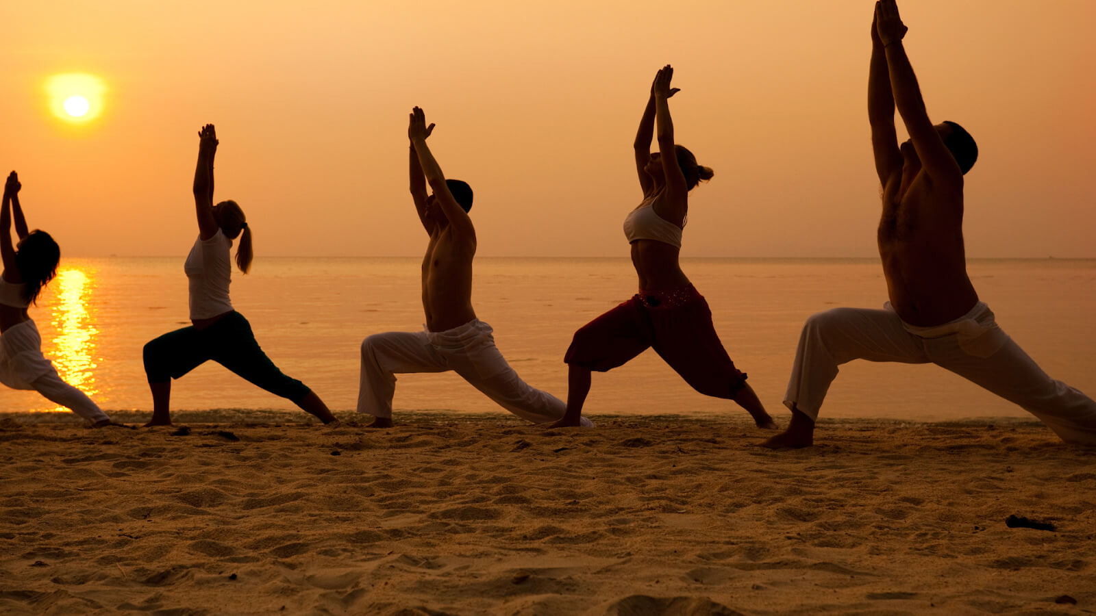 people doing yoga on a beach with sunset